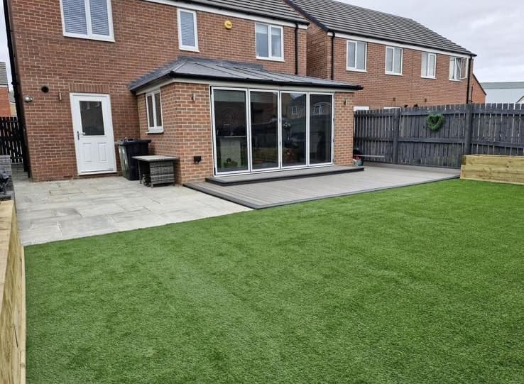 A garden lawn beside a stone patio and brick house