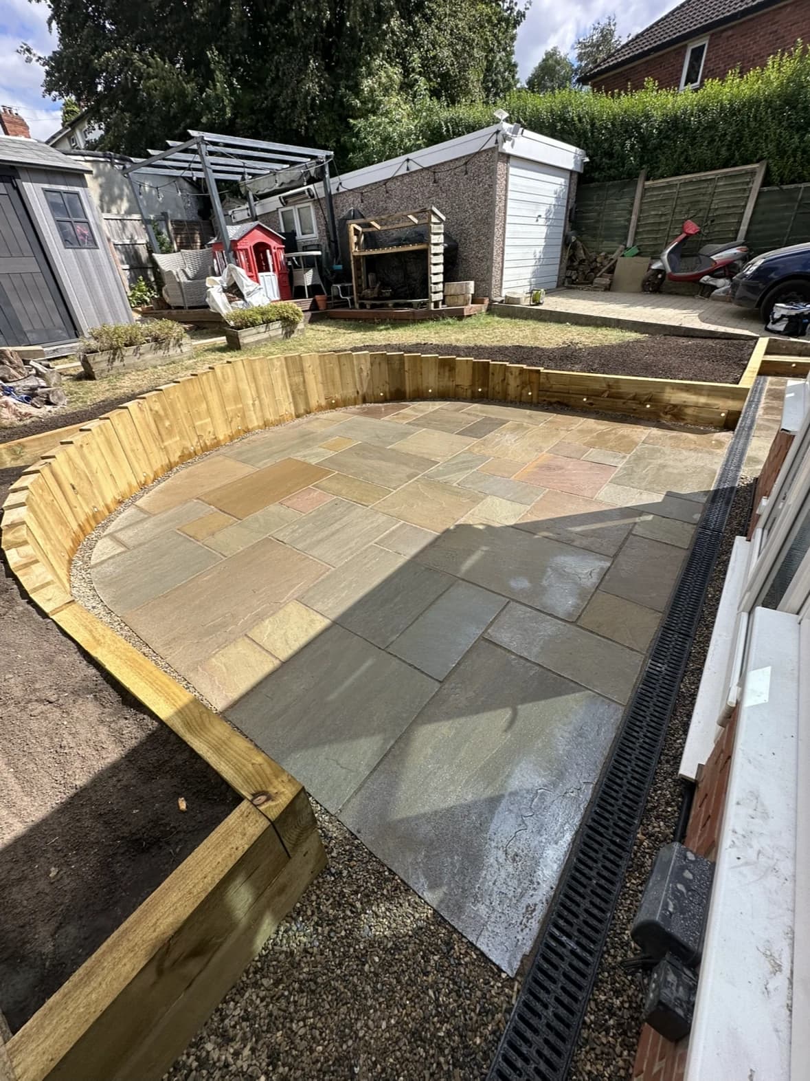 Curved stone patio with a raised timber retaining wall and drainage channel